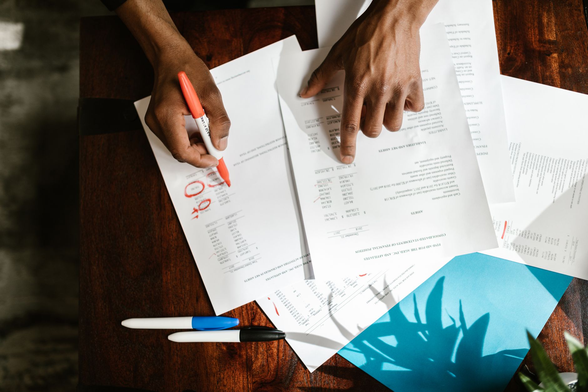 mains annotant au marqueur des documents financiers et relevés de comptes étalés sur une table, pour préparer un dossier