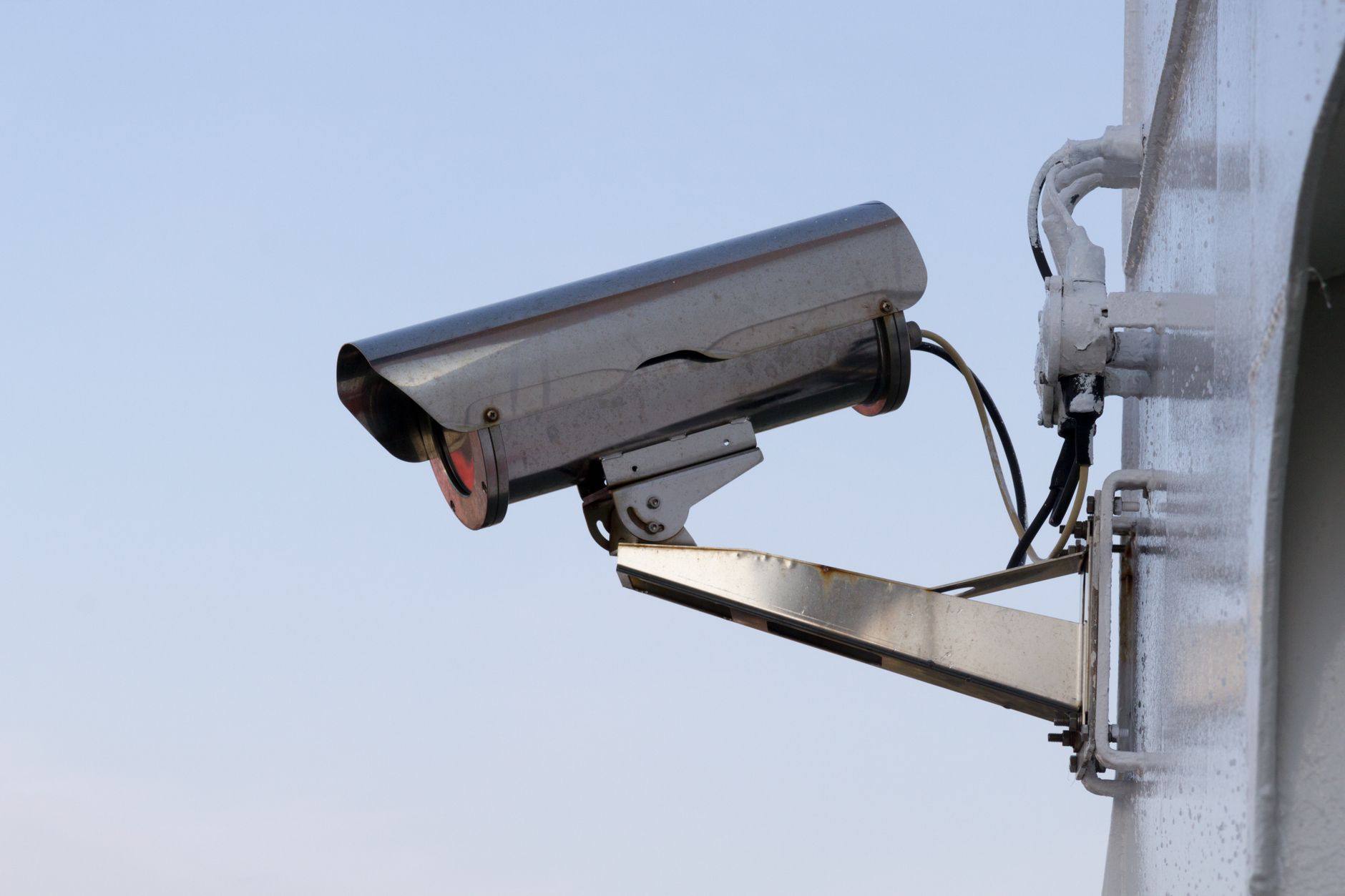 caméra de surveillance extérieure fixée sur un mur blanc, sous un ciel bleu