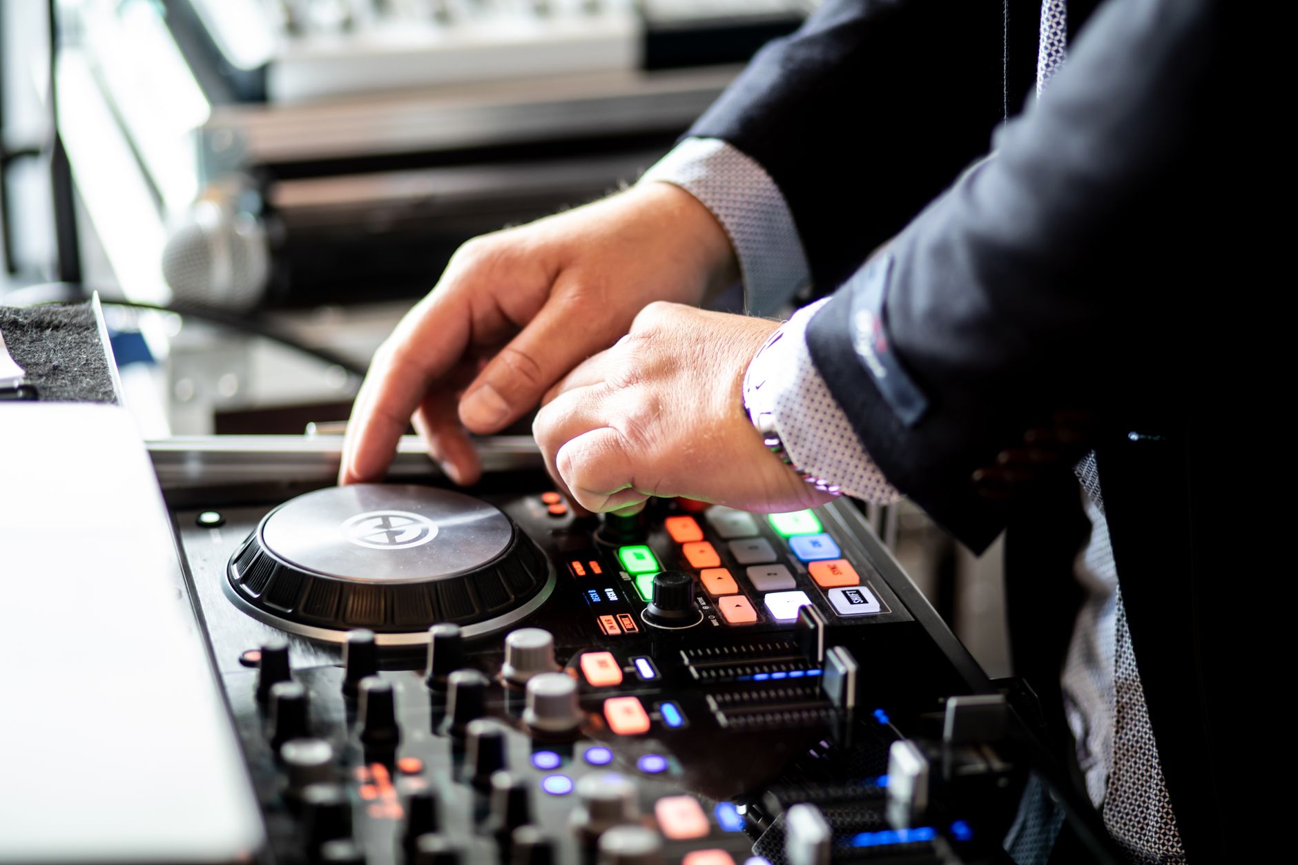 mains d'un DJ en costume sur un contrôleur de mixage éclairé
