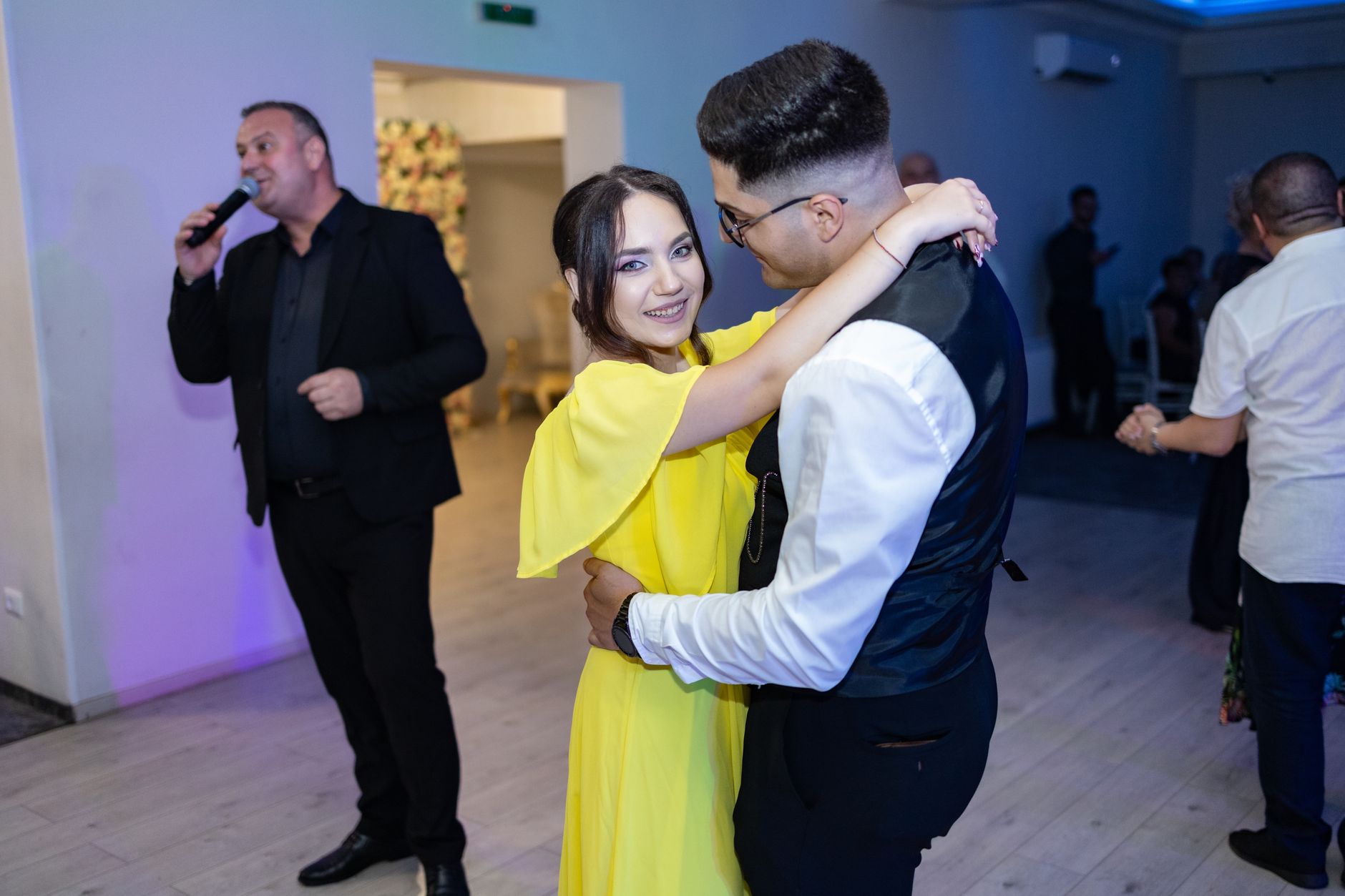 un animateur parle au micro pendant qu'un couple danse dans une salle de réception