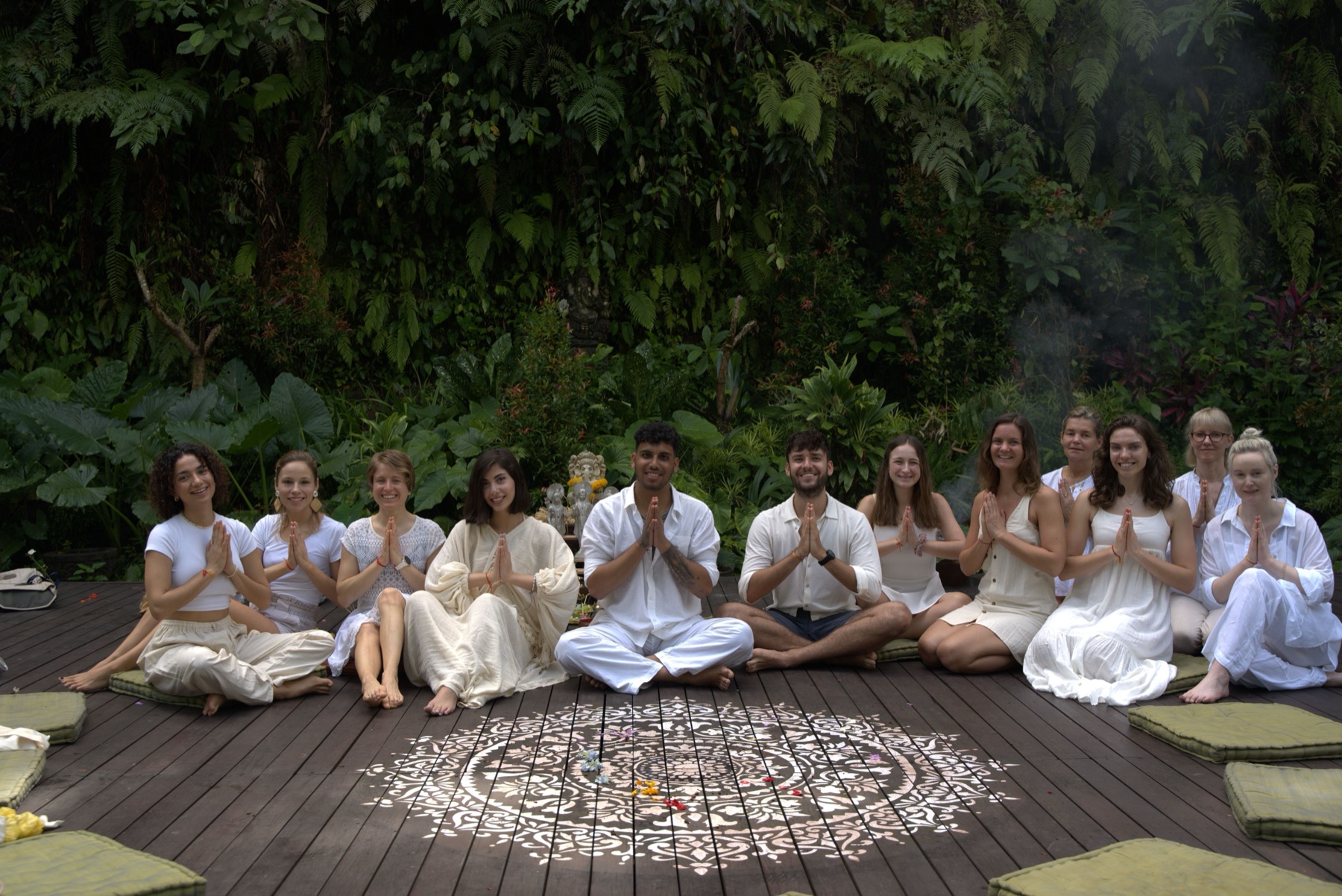 groupe assis en posture de méditation, mains jointes, dans un environnement extérieur tropical