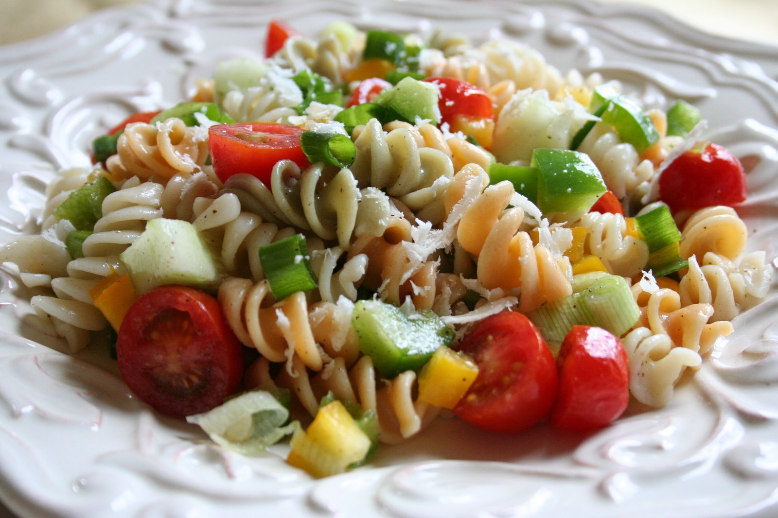 Salade de pâtes torsadées tricolores aux tomates cerises, poivron et concombre, servie froide dans une assiette blanche