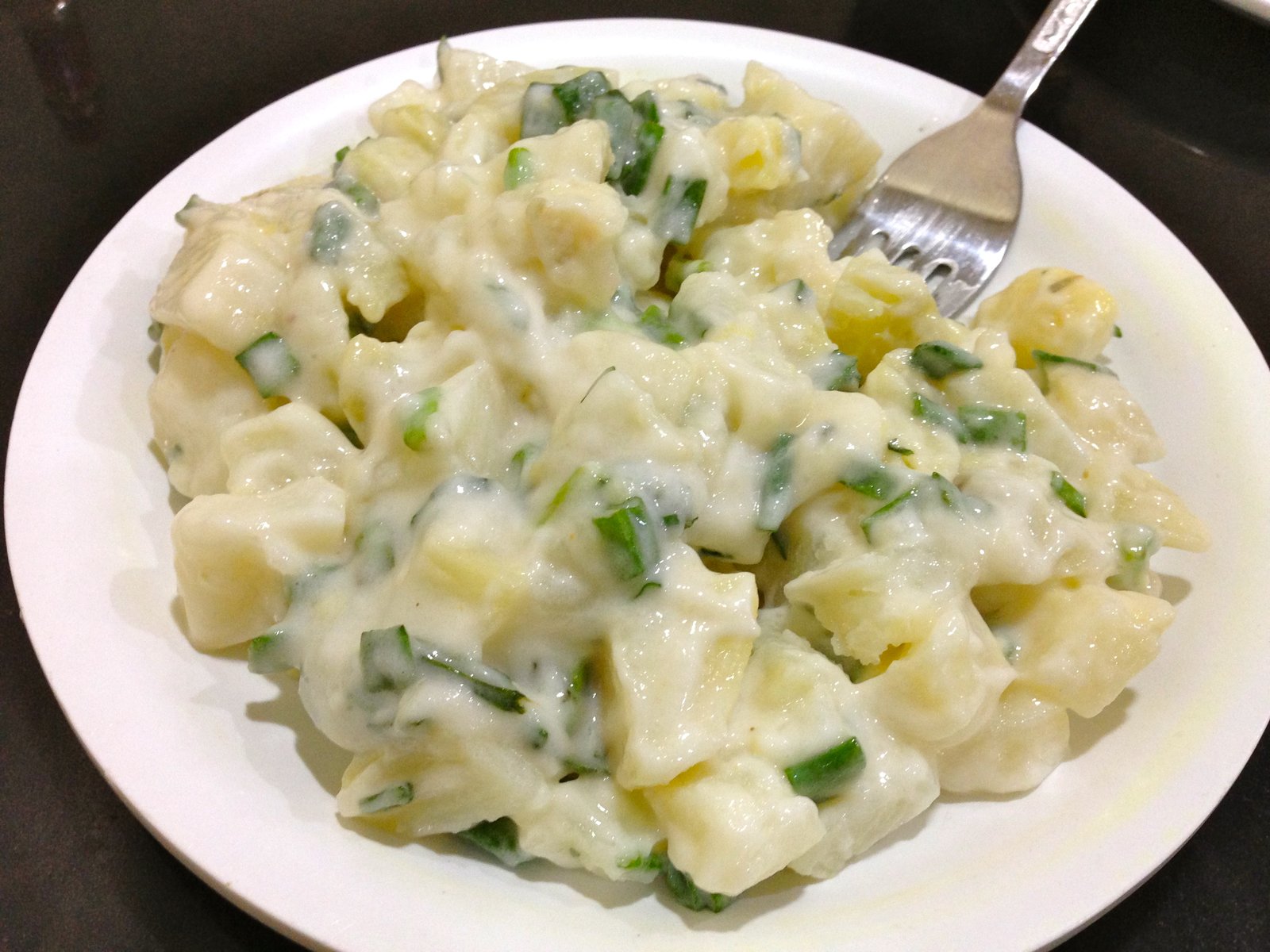 Salade de pommes de terre en dés à la crème et à la ciboulette, servie froide dans une assiette blanche avec une fourchette