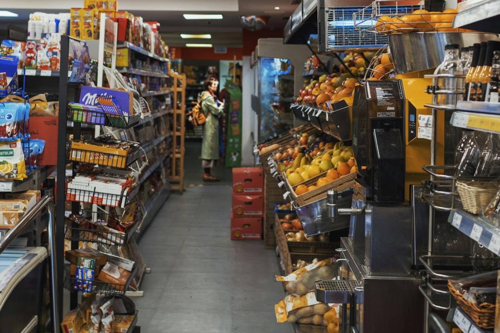 Allée de magasin avec une cliente et son panier entre deux rayons garnis