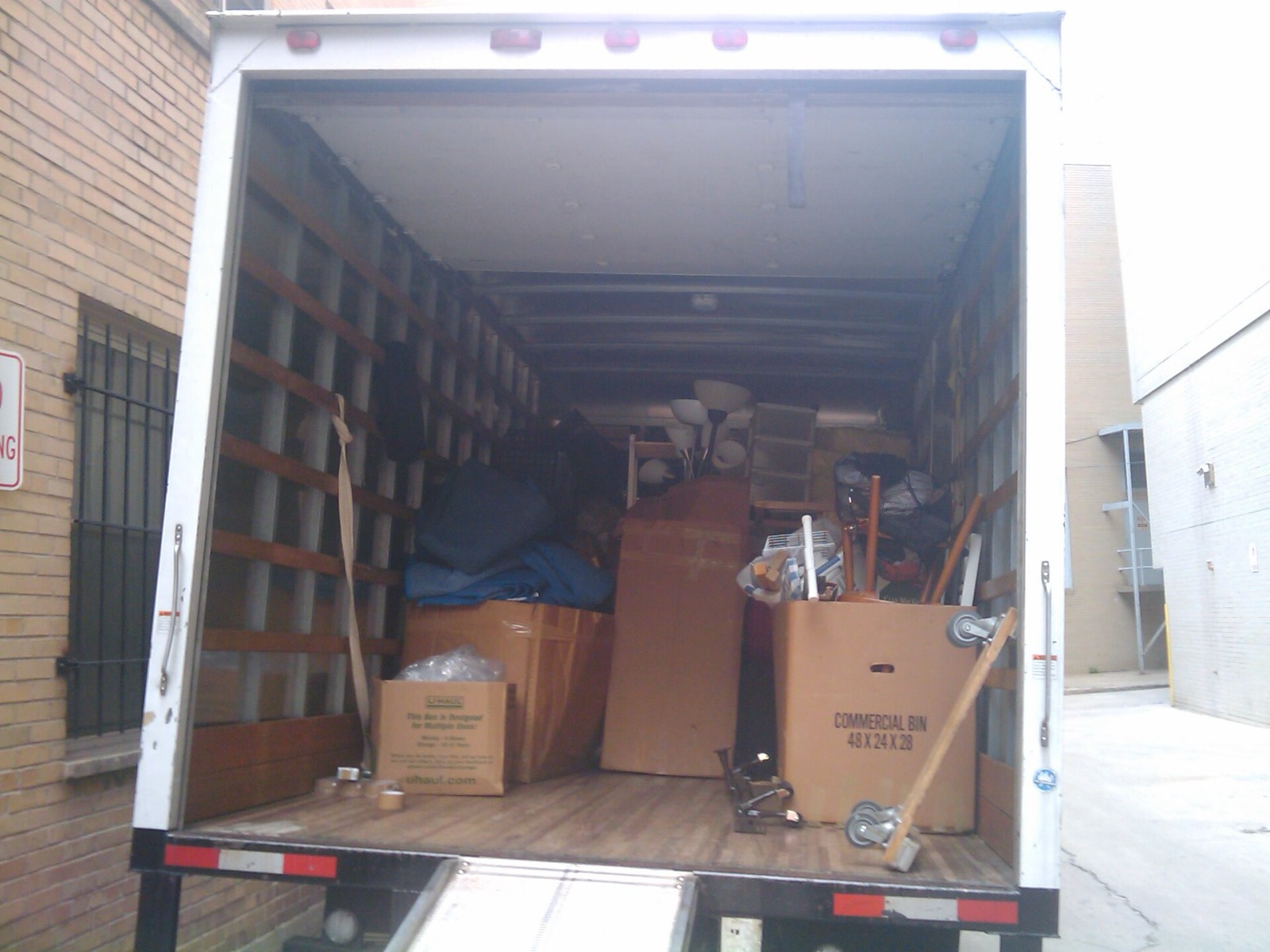 Caisse d'un camion de déménagement remplie de cartons et de meubles jusqu'au plafond, porte arrière ouverte
