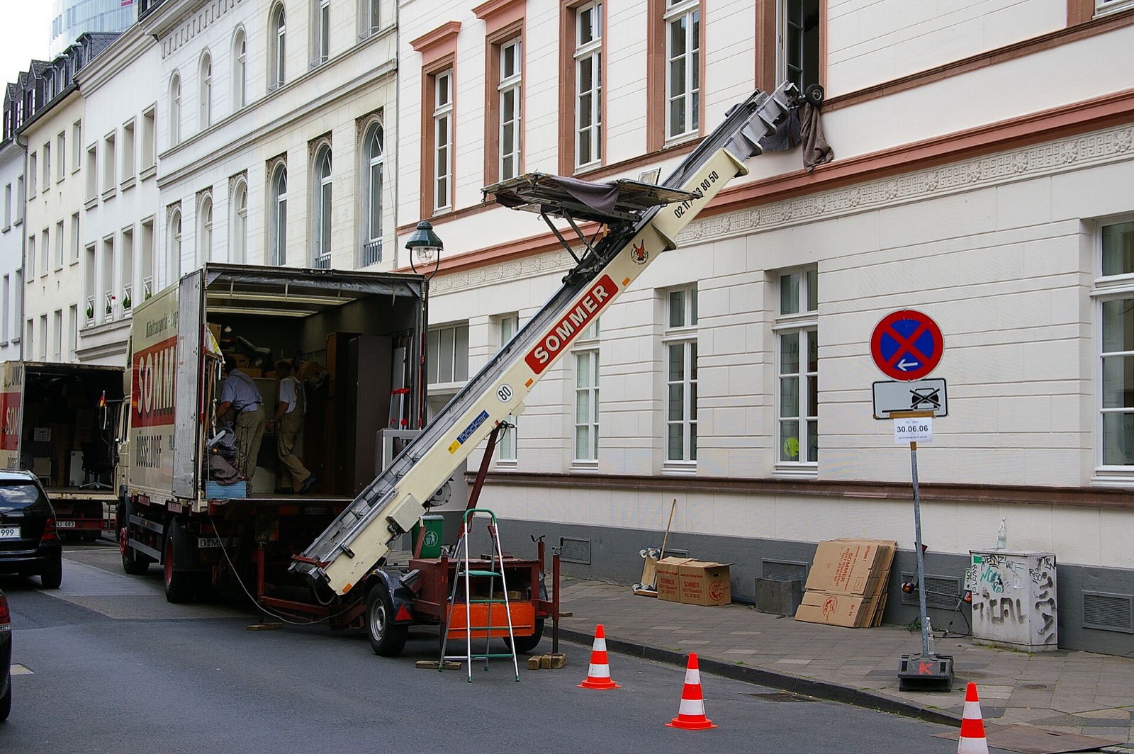 Monte-meuble déployé contre la façade d'un immeuble, camion de déménagement garé au pied et plots de signalisation sur la chaussée